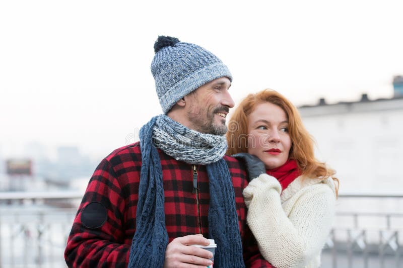 Portrait of men holding coffee cup and happy. Couple has date on city street. Loving couple looking to right way. Woman puts her hands on men shoulder. Lady feels strong men shoulder. Portrait of men holding coffee cup and happy. Couple has date on city street. Loving couple looking to right way. Woman puts her hands on men shoulder. Lady feels strong men shoulder