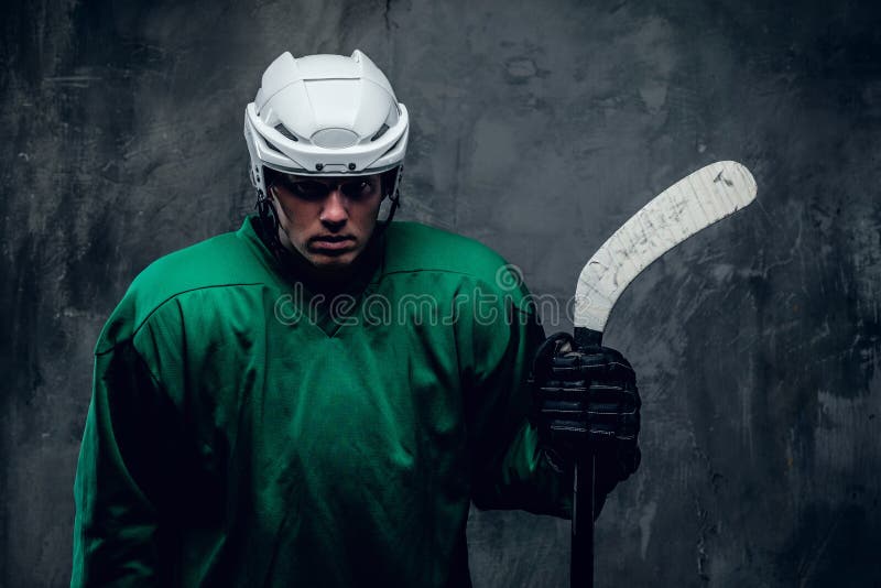 Portrait of tired hockey player in protective uniform in a shadow on grey background. Portrait of tired hockey player in protective uniform in a shadow on grey background.