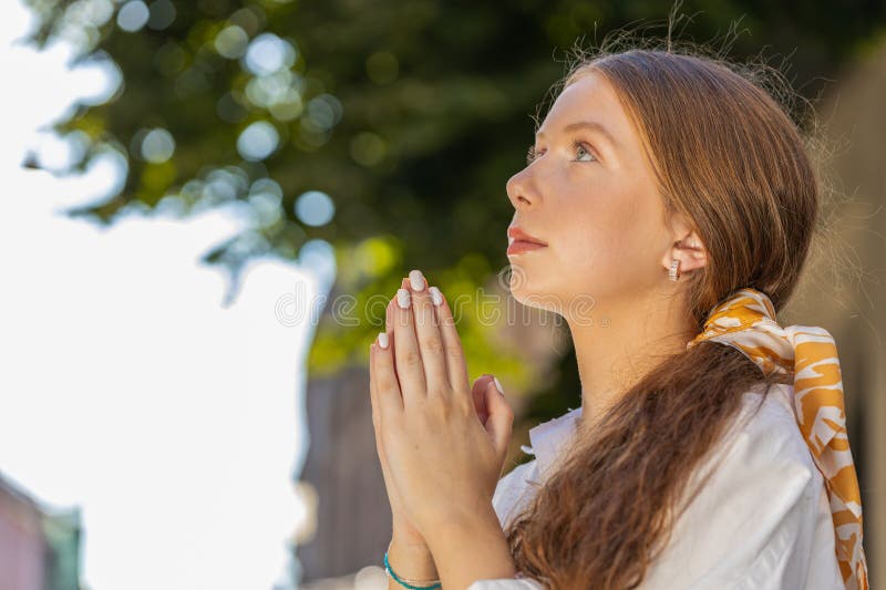 Portrait of redhead religion teenager girl praying closed eyes to God asking for blessing, help, forgiveness outdoor. Young woman clasping hands wishing luck in urban sunny city street. Town lifestyle. Portrait of redhead religion teenager girl praying closed eyes to God asking for blessing, help, forgiveness outdoor. Young woman clasping hands wishing luck in urban sunny city street. Town lifestyle