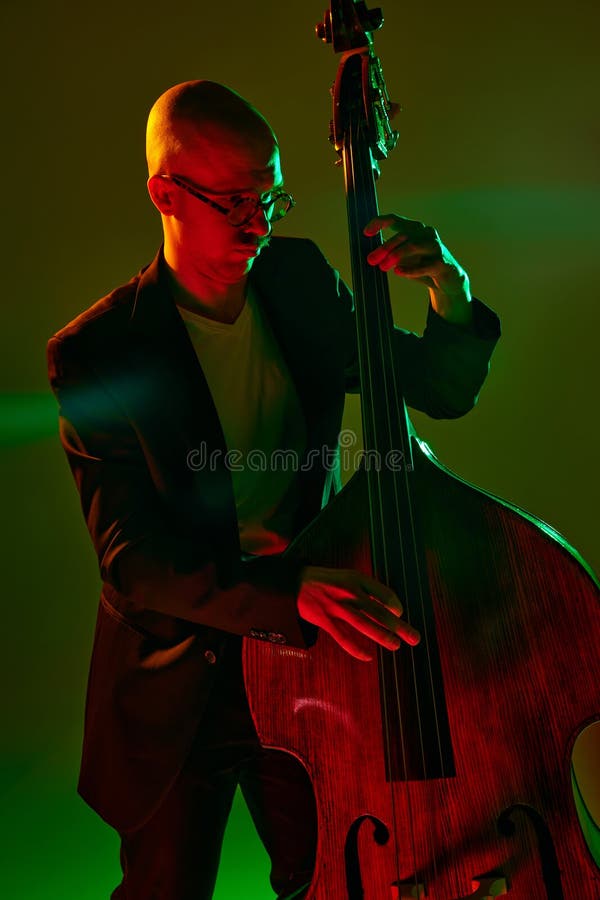 Portrait of bald musician in glasses plays double bass in red-green neon light against gradient studio background. Concept of music and art, hobby, concerts and festivals, modern culture. Ad. Portrait of bald musician in glasses plays double bass in red-green neon light against gradient studio background. Concept of music and art, hobby, concerts and festivals, modern culture. Ad