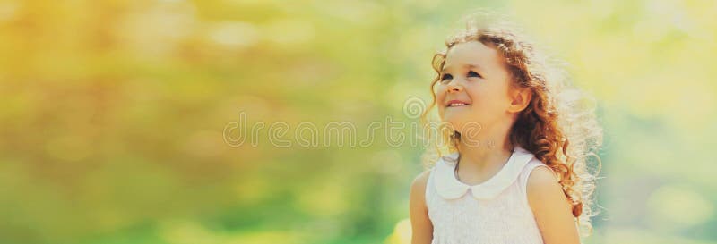 πορτραίτο χαρούμενου χαμογελαστού μικρού κοριτσιού με σγουρά μαλλιά που κοιτούν ψηλά το ηλιόλουστο καλοκαίρι, κενό διάστημα για