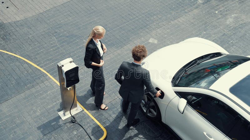 προοδευτικός επιχειρηματίας και επιχειρηματίας που κλίνει πάνω στο αυτοκίνητο και το σημείο φόρτισης. στοκ εικόνες