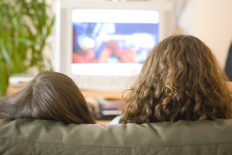 Two girls sit watching tv. Two girls sit watching tv