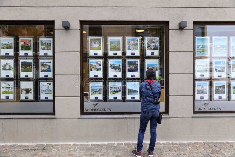 MANDAL, NORWAY - JULY 17, 2020: Person analyzes real estate offers of a real estate agency window in town of Mandal in Vest-Agder county of Norway. MANDAL, NORWAY - JULY 17, 2020: Person analyzes real estate offers of a real estate agency window in town of Mandal in Vest-Agder county of Norway