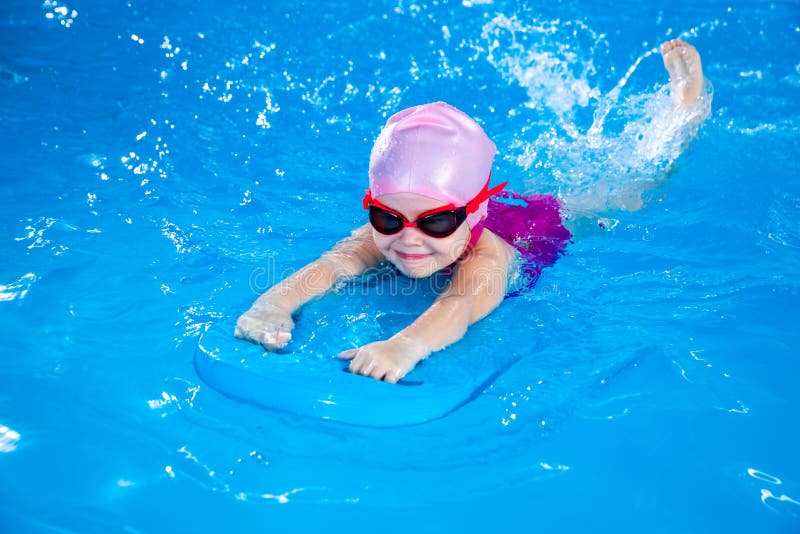 προσχολική χαριτωμένη κοπέλα μαθαίνει να κολυμπά στην εσωτερική πισίνα με σανίδα