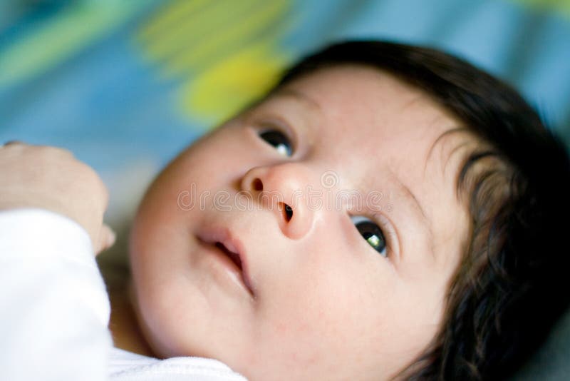 Image of a little cute mixed-blood infant baby boy lying on bed with his eyes open, he is half caucasian and half chinese and only one month old. Image of a little cute mixed-blood infant baby boy lying on bed with his eyes open, he is half caucasian and half chinese and only one month old