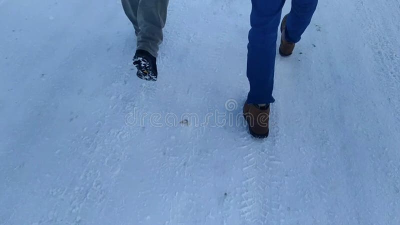 πόδια δύο νέων που περπατάνε σε ένα χιονισμένο δρόμο τη μέρα. φιλμ μικρού μήκους