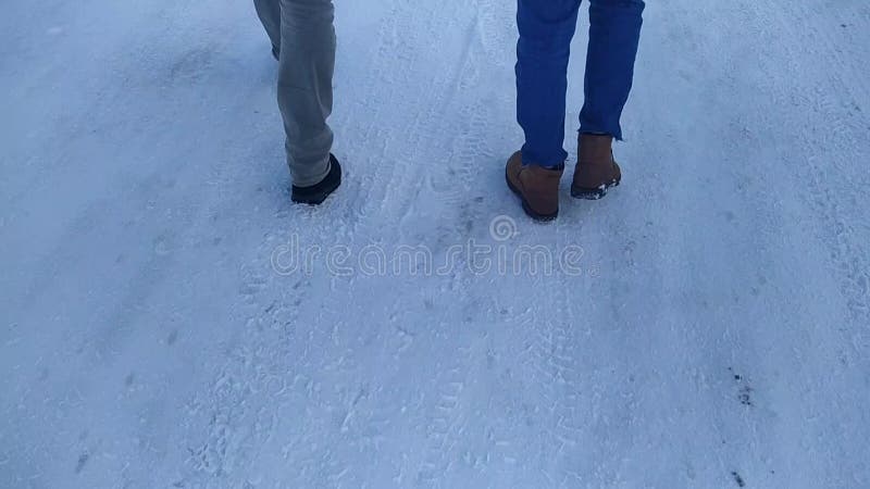 πόδια δύο νέων που περπατάνε σε ένα χιονισμένο δρόμο τη μέρα. απόθεμα βίντεο
