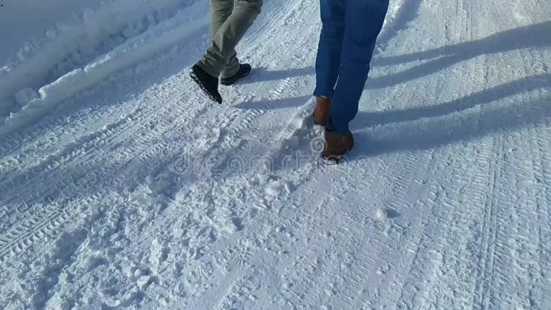 πόδια δύο νέων που περπατάνε σε ένα χιονισμένο δρόμο τη μέρα. απόθεμα βίντεο