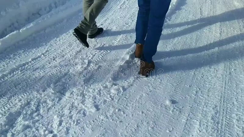 πόδια δύο νέων που περπατάνε σε ένα χιονισμένο δρόμο τη μέρα. φιλμ μικρού μήκους