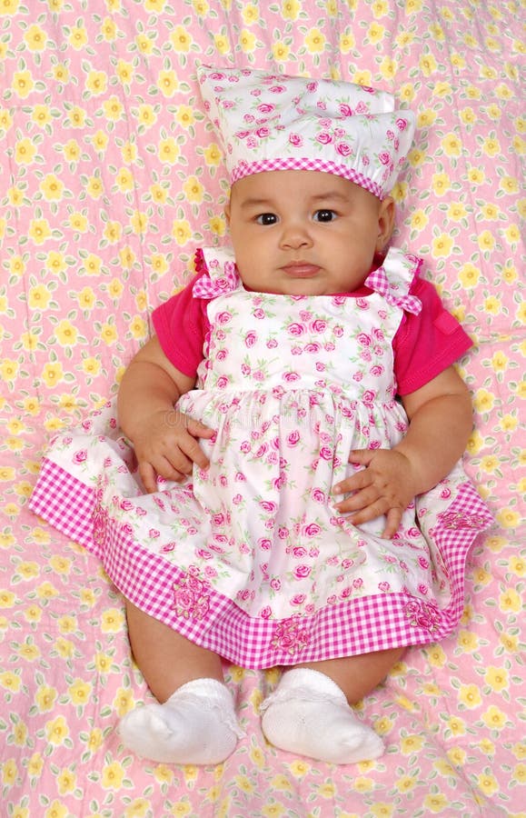 Vertical portrait of a 3-month-old baby girl in a pink flowery dress sitting on a pink blanket with yellow flower pattern. Vertical portrait of a 3-month-old baby girl in a pink flowery dress sitting on a pink blanket with yellow flower pattern