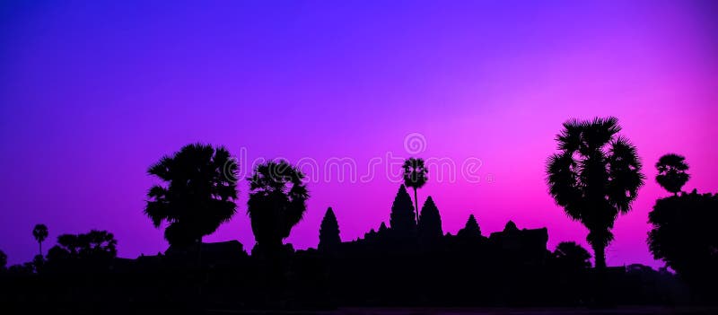 Panorama Palm trees Mist sunrise tropical morning violet tourist attraction ancient temple facade silhouette of the Angkor Wat temple in Angkor Archaeological Park near Siem Reap in Cambodia. Panorama Palm trees Mist sunrise tropical morning violet tourist attraction ancient temple facade silhouette of the Angkor Wat temple in Angkor Archaeological Park near Siem Reap in Cambodia.