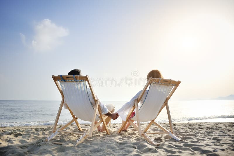 Ρομαντικό ζεύγος στο deckchair που χαλαρώνει απολαμβάνοντας το ηλιοβασίλεμα στην παραλία στοκ εικόνες