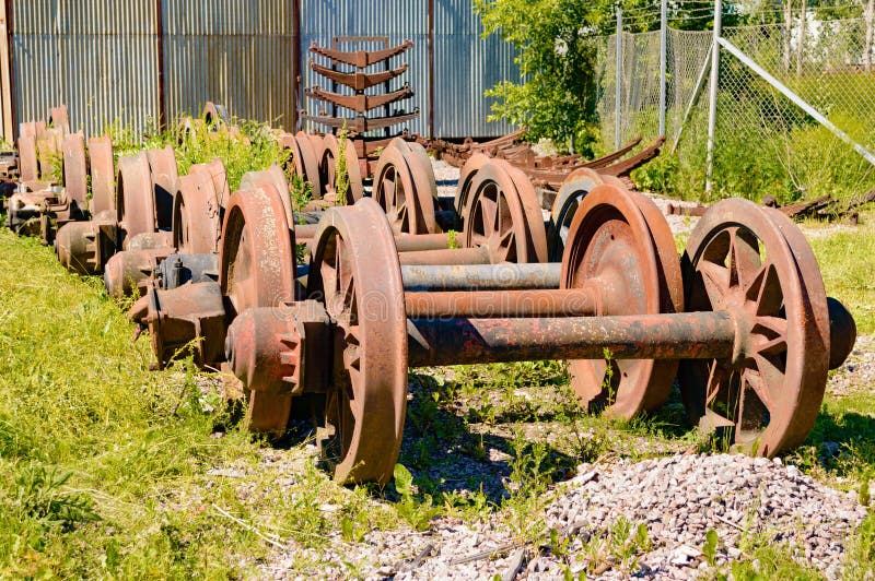 A stockpile of old, rusty and abandoned train wheels lying in the grass close to train service depot. A stockpile of old, rusty and abandoned train wheels lying in the grass close to train service depot.