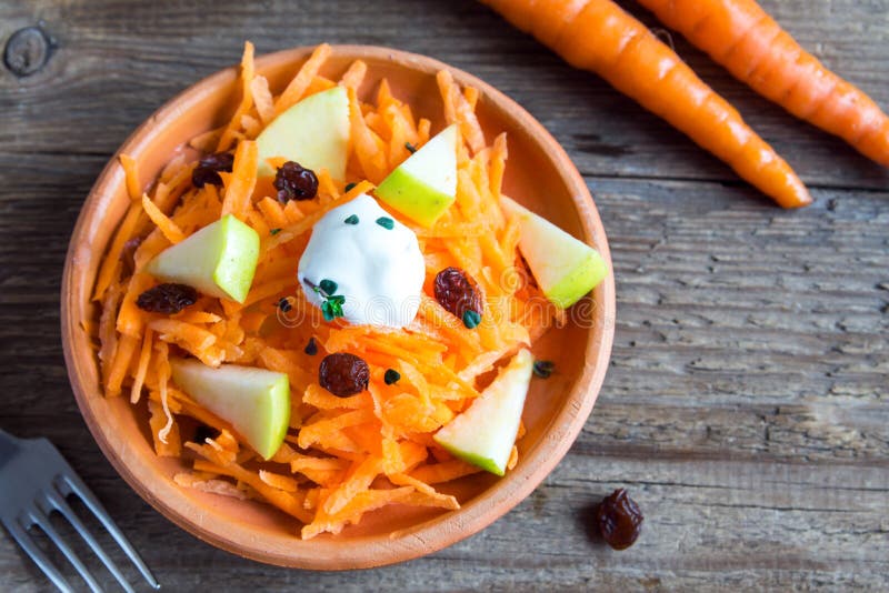 Carrot and apple salad with raisins, yogurt and herbs in rustic ceramic bowl, copy space. Carrot and apple salad with raisins, yogurt and herbs in rustic ceramic bowl, copy space