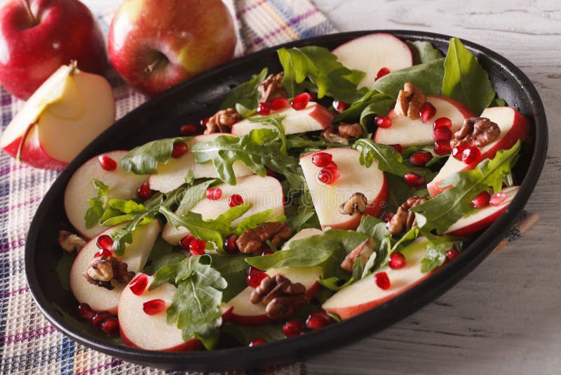 Apple salad with pomegranate, walnuts and arugula close-up on the table. horizontal. Apple salad with pomegranate, walnuts and arugula close-up on the table. horizontal