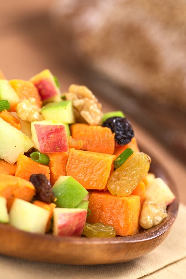 Fresh salad made of cooked sweet potatoes, fresh apples, nuts, raisins and shallots on wooden plate with wholewheat bread in the back (Selective Focus, Focus one third into the salad). Fresh salad made of cooked sweet potatoes, fresh apples, nuts, raisins and shallots on wooden plate with wholewheat bread in the back (Selective Focus, Focus one third into the salad)