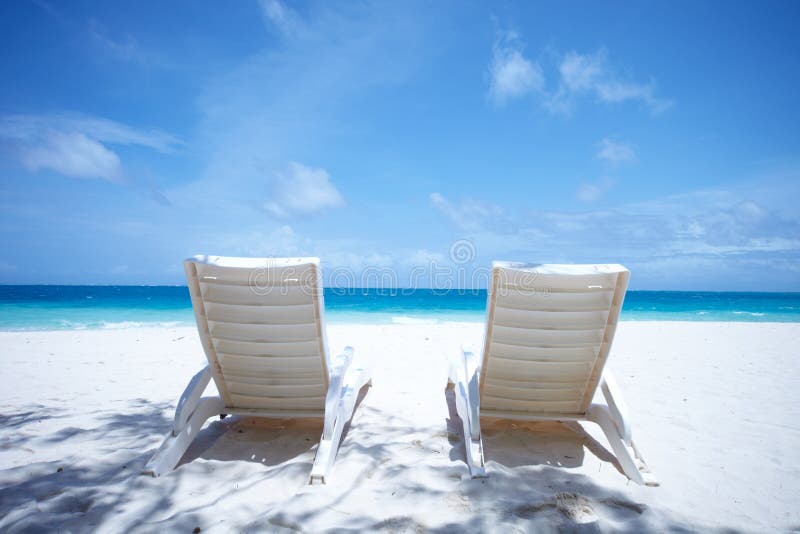 Unoccupied lounge chairs wait for someone to sit in them on a sun drenched tropical beach. Unoccupied lounge chairs wait for someone to sit in them on a sun drenched tropical beach.