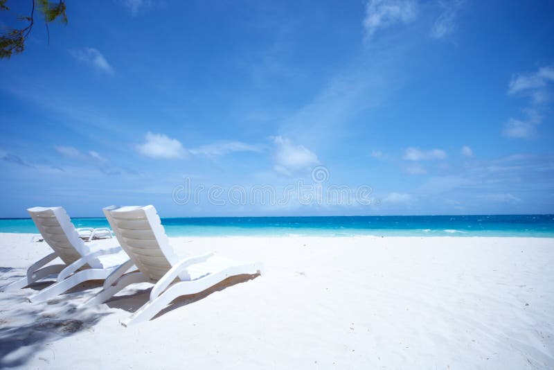 Unoccupied lounge chairs wait for someone to sit in them on a sun drenched tropical beach. Unoccupied lounge chairs wait for someone to sit in them on a sun drenched tropical beach.