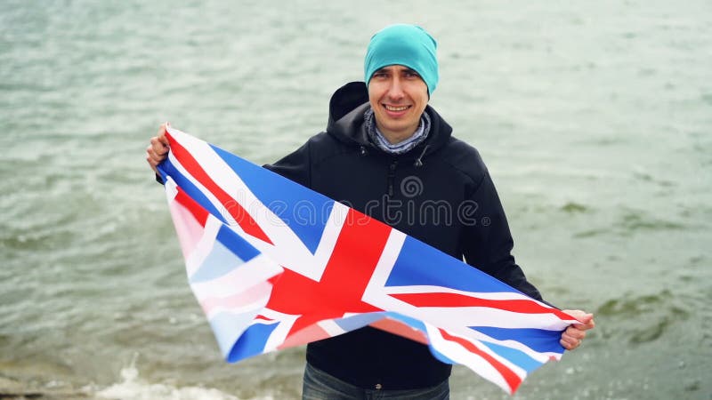 Σε αργή κίνηση πορτρέτο της πατριωτικής σημαίας εκμετάλλευσης Άγγλου της Μεγάλης Βρετανίας που στέκεται στην παραλία και που χαμο