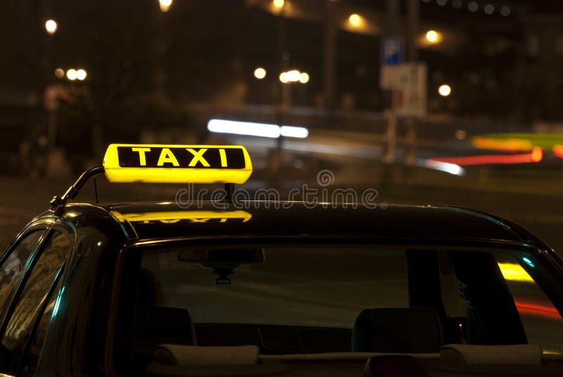 A photo of a taxi sign on a top of a taxi car at night. A photo of a taxi sign on a top of a taxi car at night.