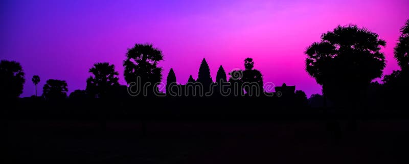 Panorama Mist sunrise tropical morning violet mauve sky landscape. Palm trees Famous facade silhouette of Cambodian ancient temple Angkor wat, Angkor Archaeological Park near Siem Reap in Cambodia. Panorama Mist sunrise tropical morning violet mauve sky landscape. Palm trees Famous facade silhouette of Cambodian ancient temple Angkor wat, Angkor Archaeological Park near Siem Reap in Cambodia