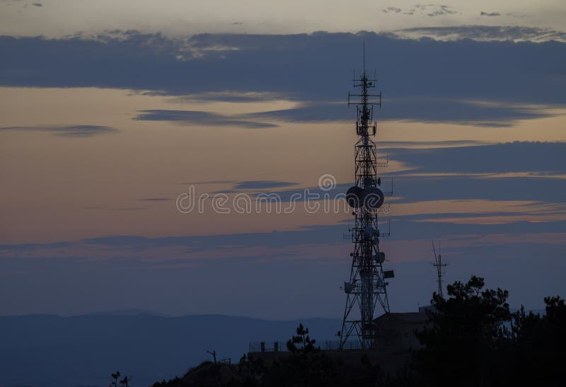 Σιλουέτα πύργου τηλεπικοινωνιών στο ηλιοβασίλεμα που φωτίζει πολύχρωμα σύννεφα στοκ εικόνες