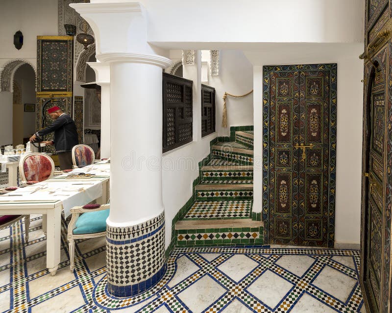 Pictured is the staircase leading to the breakfast room of the Riad Maison Bleue, a luxury boutique hotel in Fes, Morocco. A waiter with a red fez is pouring coffee for a quest.  Beautiful carved wooden doors and a mosaic tile floor are also seen.  The Riad Maison Bleue was created in a house dating from the 19th century whose former owner, was the late Moulay Bel Arbi El Alaoui, famous judge and professor of theology. Today the luxury boutique hotel it is managed by the El Abbadi`s family. Pictured is the staircase leading to the breakfast room of the Riad Maison Bleue, a luxury boutique hotel in Fes, Morocco. A waiter with a red fez is pouring coffee for a quest.  Beautiful carved wooden doors and a mosaic tile floor are also seen.  The Riad Maison Bleue was created in a house dating from the 19th century whose former owner, was the late Moulay Bel Arbi El Alaoui, famous judge and professor of theology. Today the luxury boutique hotel it is managed by the El Abbadi`s family.