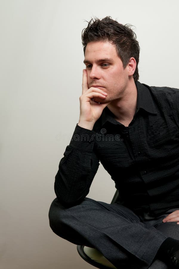 Young man in black clothes sitting on a chair and thinking. Young man in black clothes sitting on a chair and thinking