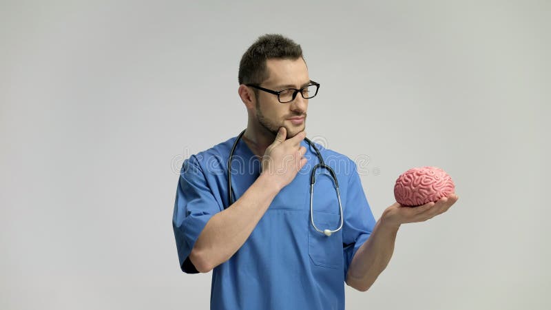 Σκεπτικός γιατρός που κρατά ένα πρότυπο εγκεφάλου και που δείχνει επάνω με το δάχτυλό του