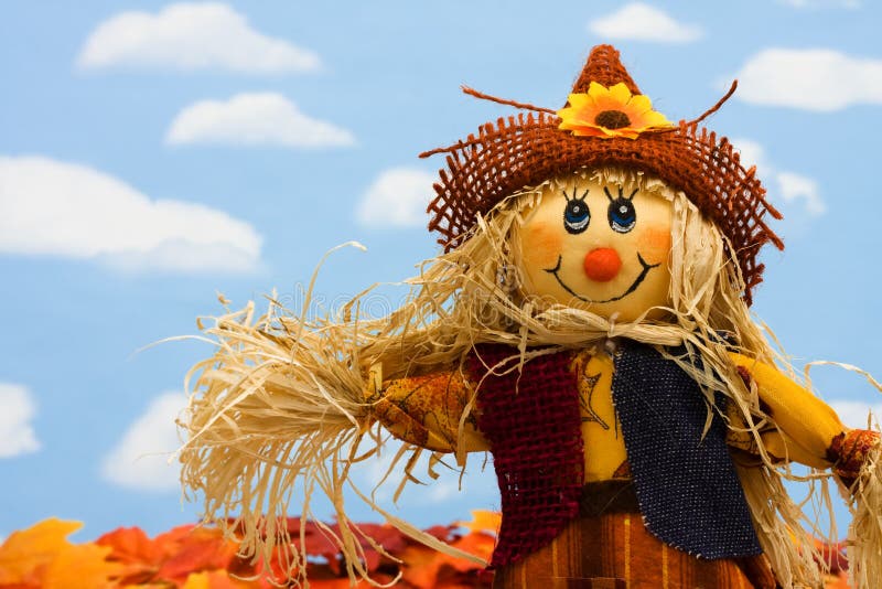 A scarecrow sitting on fall leaves on a sky background, scarecrow. A scarecrow sitting on fall leaves on a sky background, scarecrow