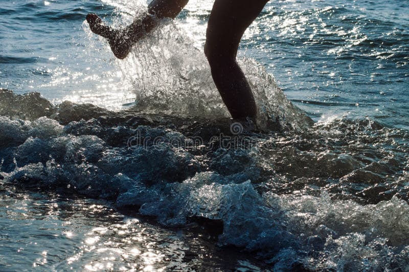 Σκιαγραφία ενός νέου, λεπτού, προκλητικού καταβρέχοντας νερού ποδιών γυναικών στη θάλασσα στο ηλιοβασίλεμα στοκ εικόνες
