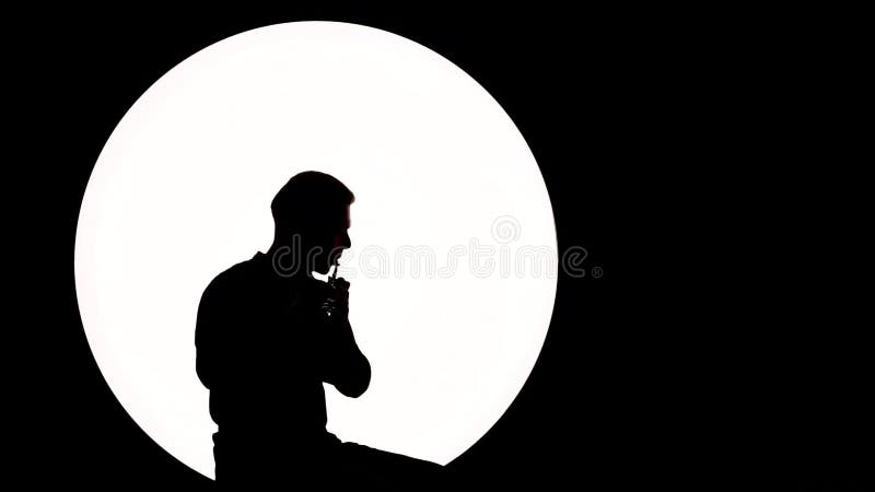 Σκιαγραφία ενός τύπος-μουσικού Ένας νεαρός άνδρας παίζει το φλάουτο καθμένος σε ένα άσπρο υπόβαθρο κύκλων ως πανσέληνος απόθεμα βίντεο