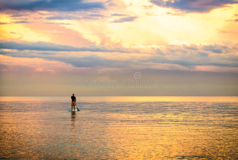 A sunset Silhouette of a man on stand up paddle board with golden sea and clouds. A sunset Silhouette of a man on stand up paddle board with golden sea and clouds.