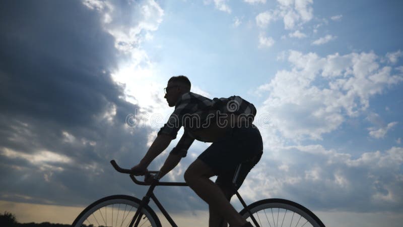 Σκιαγραφία της οδήγησης νεαρών άνδρων στο εκλεκτής ποιότητας ποδήλατο με τον όμορφο ουρανό ηλιοβασιλέματος στο υπόβαθρο Φίλαθλη α στοκ εικόνες με δικαίωμα ελεύθερης χρήσης Σκιαγραφία της οδήγησης νεαρών άνδρων στο εκλεκτής ποιότητας ποδήλατο με τον όμορφο ουρανό ηλιοβασιλέματος στο υπόβαθρο Φίλαθλη α στοκ εικόνες με δικαίωμα ελεύθερης χρήσης