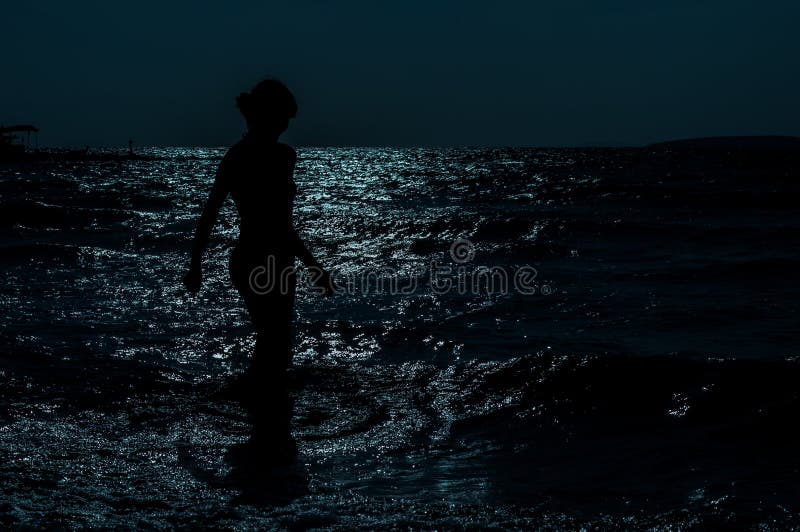 Σκιαγραφία του νέου, λεπτού, προκλητικού περπατήματος γυναικών στη θάλασσα κάτω από το σεληνόφωτο στοκ εικόνα