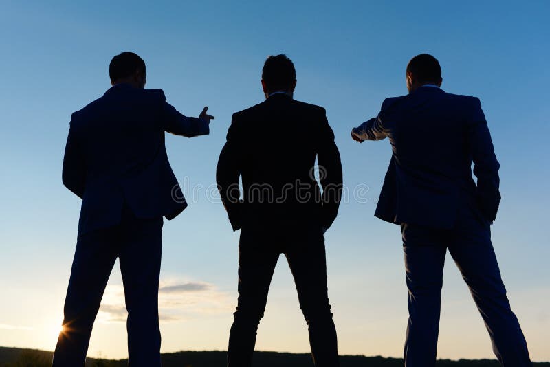 Silhouettes of company leaders standing on sunset sky background. Board of executives look at their worksite and new goals. Businessmen figures in formal suits. Business success and leadership concept. Silhouettes of company leaders standing on sunset sky background. Board of executives look at their worksite and new goals. Businessmen figures in formal suits. Business success and leadership concept