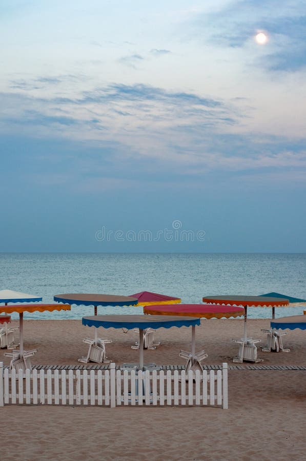 Σκοτεινό seascape με τις ζωηρόχρωμες ομπρέλες παραλιών και τον άσπρο ξύλινο φράκτη στοκ εικόνες με δικαίωμα ελεύθερης χρήσης