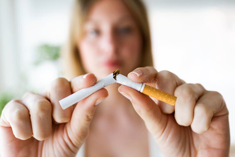 Σοβαρή νέα γυναίκα που σπάζει ένα τσιγάρο στο σπίτι Έννοια εθισμού στοκ φωτογραφία Σοβαρή νέα γυναίκα που σπάζει ένα τσιγάρο στο σπίτι Έννοια εθισμού στοκ φωτογραφία