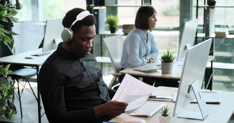 σοβαρός αφρικανός αμερικανός επιχειρηματίας εστιάζει στην εργασία ενώ ακούει μουσική με εφημερίδες
