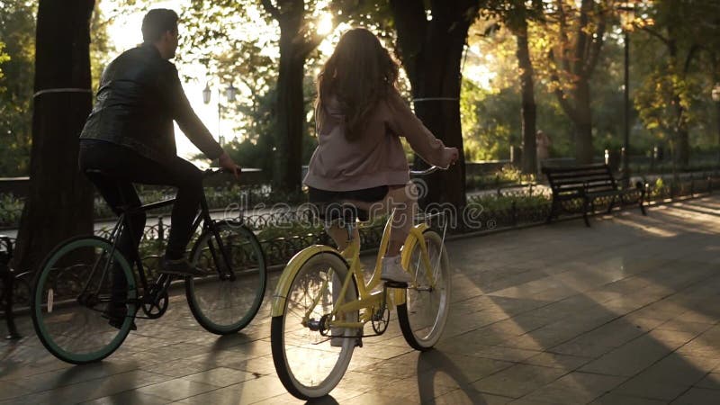 Σπάνια άποψη του καυκάσιων νέων ζεύγους ή των φίλων που οδηγά τα ποδήλατά τους στο κενή πάρκο ή τη λεωφόρο πόλεων στο καλοκαίρι
