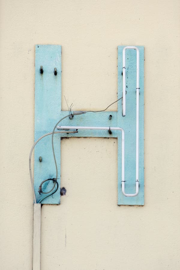 Broken neon sign blue letter H on beige wall. Broken neon sign blue letter H on beige wall