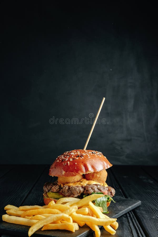 Σπιτικό juicy burger με τις τηγανιτές πατάτες στο σκοτεινό ξύλινο πίνακα στοκ εικόνα Σπιτικό juicy burger με τις τηγανιτές πατάτες στο σκοτεινό ξύλινο πίνακα στοκ εικόνα