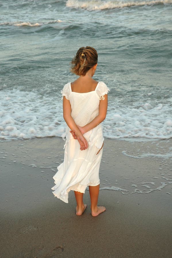 Little girl stands out on the sand of the ocean as teh sun sets behind her and watches the crashing waves. Little girl stands out on the sand of the ocean as teh sun sets behind her and watches the crashing waves.