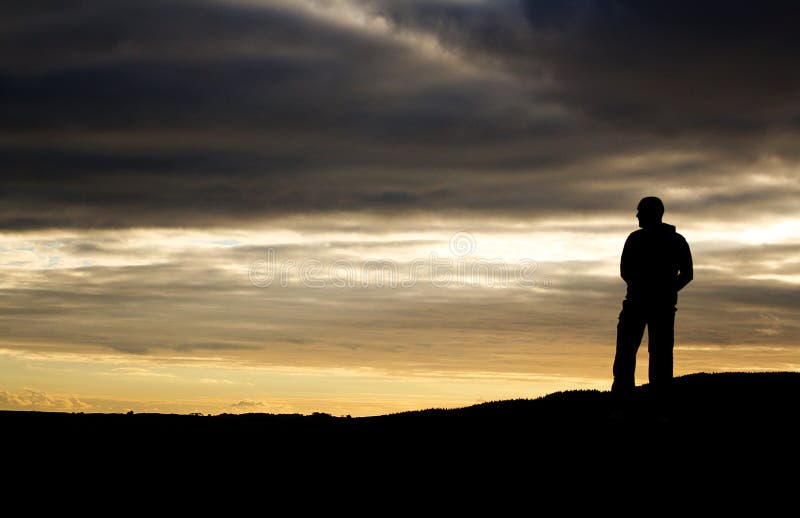 Sillouette of a man standing on a mountain as the sun sets. Sillouette of a man standing on a mountain as the sun sets