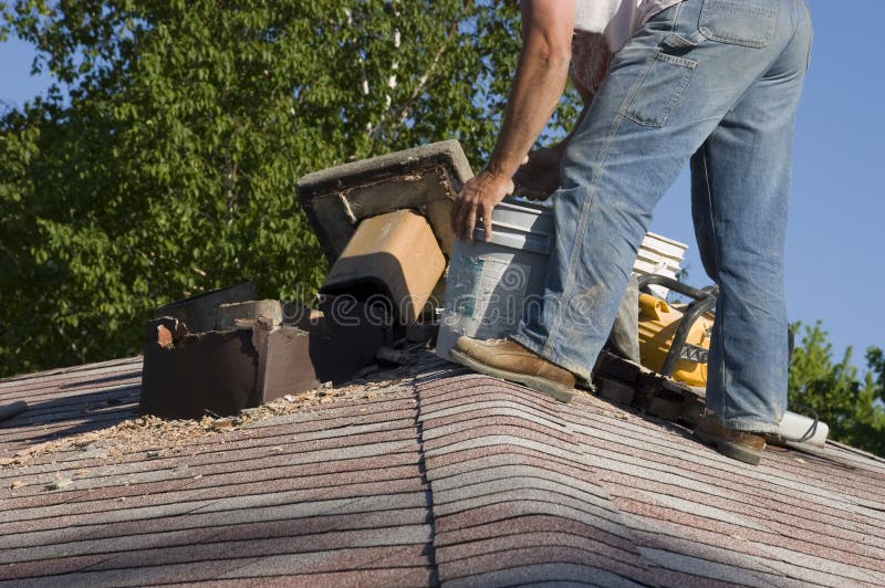 House chimney has been torn down and rests on the roof as the structure is being repaired. One of many aspects for home repair and house maintenance. The bricks need to be replaced by a mason or bricklayer. Construction worker can be seen as he works. House chimney has been torn down and rests on the roof as the structure is being repaired. One of many aspects for home repair and house maintenance. The bricks need to be replaced by a mason or bricklayer. Construction worker can be seen as he works.