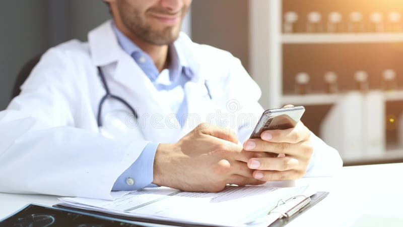 στενή αρσενική γιατρός με λευκή στολή κρατά αναζήτηση smartphone στο διαδίκτυο σε κλινική. φιλμ μικρού μήκους