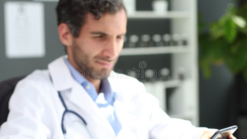 στενή αρσενική γιατρός με λευκή στολή κρατά αναζήτηση smartphone στο διαδίκτυο σε κλινική. απόθεμα βίντεο