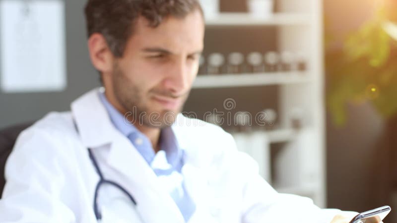 στενή αρσενική γιατρός με λευκή στολή κρατά αναζήτηση smartphone στο διαδίκτυο σε κλινική. απόθεμα βίντεο