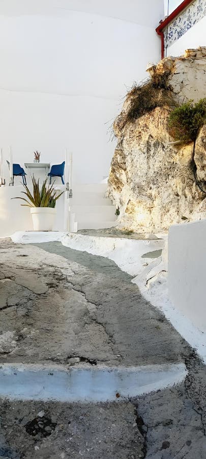 στενό μονοπάτι με ραγισμένο πεζοδρόμιο οδηγεί σε γαλάζιες καρέκλες σε λευκό τοίχο που προκαλεί γαλήνη στοκ φωτογραφία